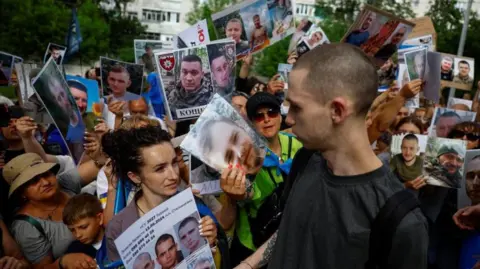 Reuters A Ukrainian prisoner of returns to a crowd of people holding posters bearing the faces of missing soldiers