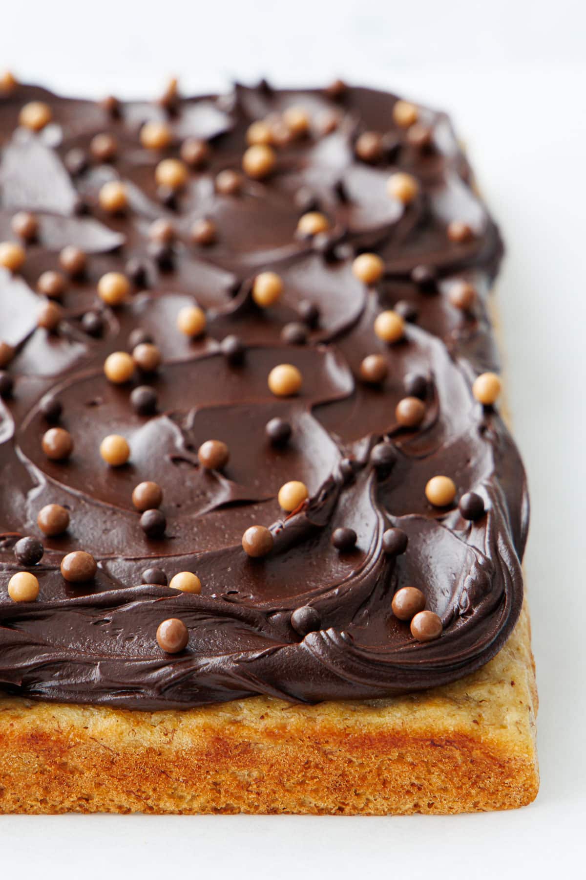 Freshly frosted Brown Butter Banana Cake with shiny swirls of Chocolate Fudge Frosting and dotted with multi-colored chocolate crisp pearls.