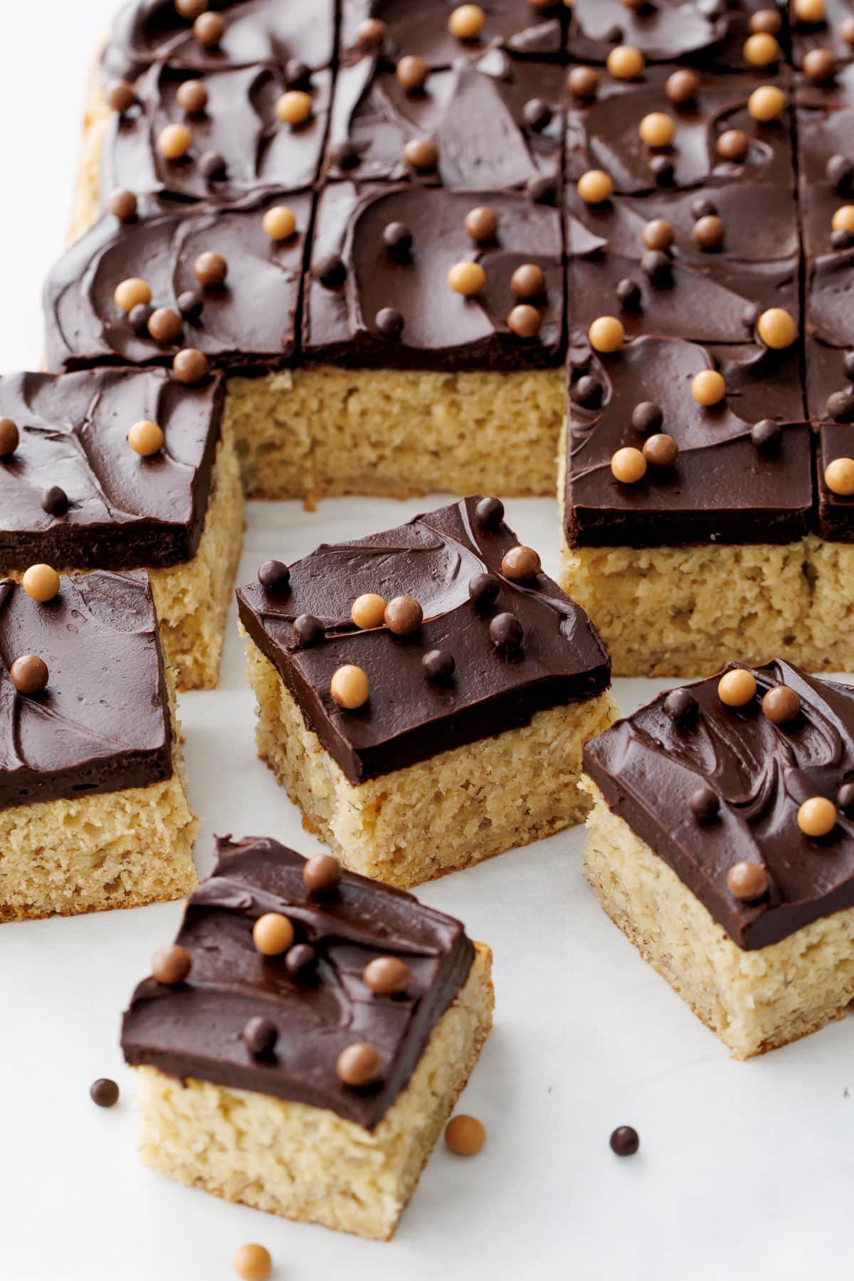 Cut squares of Brown Butter Banana Cake with Chocolate Fudge Frosting topped with multi-color crispy pearls.