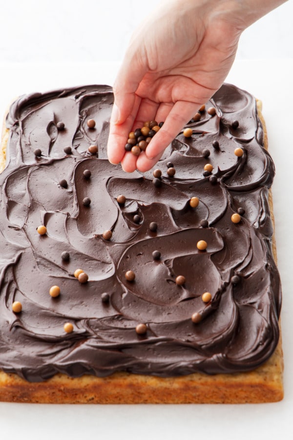 Sprinkling top of frosted cake with multi-colored chocolate crisp pearls.