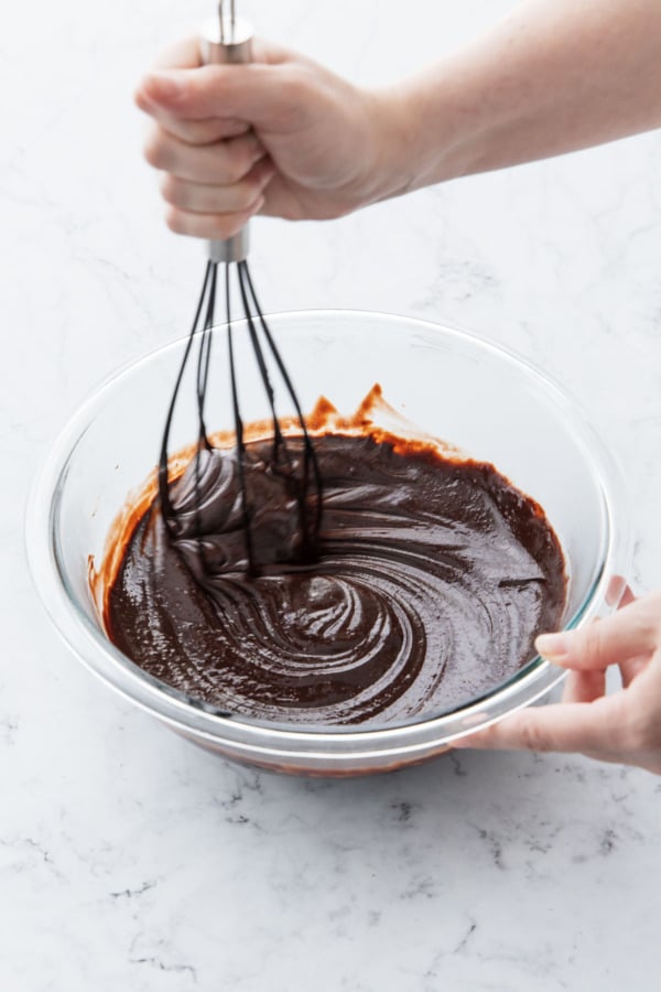 Whisking warm frosting until chocolate is fully melted and smooth.