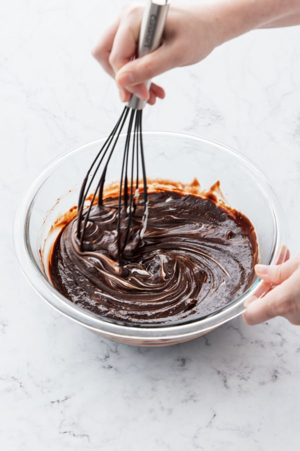 Stirring chocolate fudge frosting until shiny and smooth.