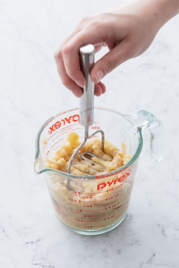 Mashing banana in a glass measuring cup with a mini potato masher.