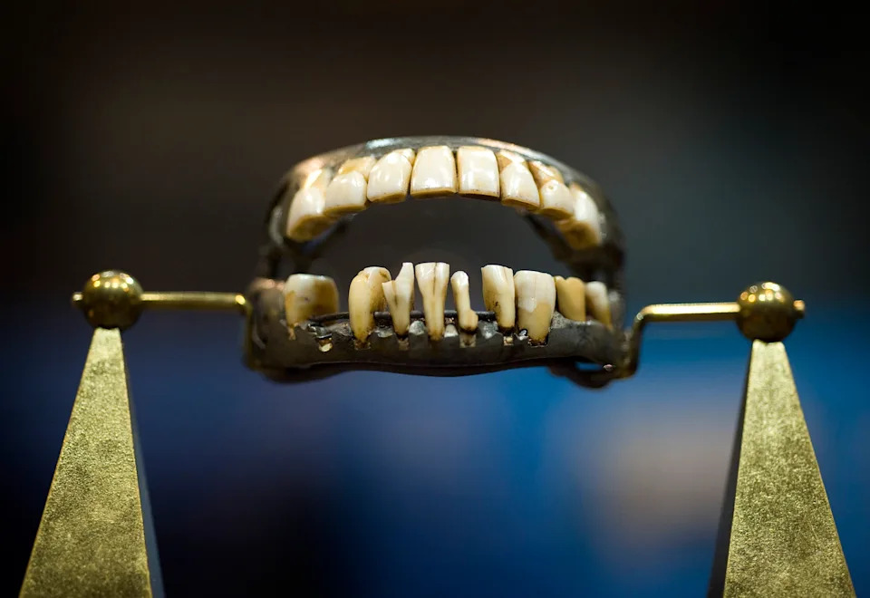 A set of worn, historically significant false teeth displayed on a gold stand, showcasing uneven and aged features