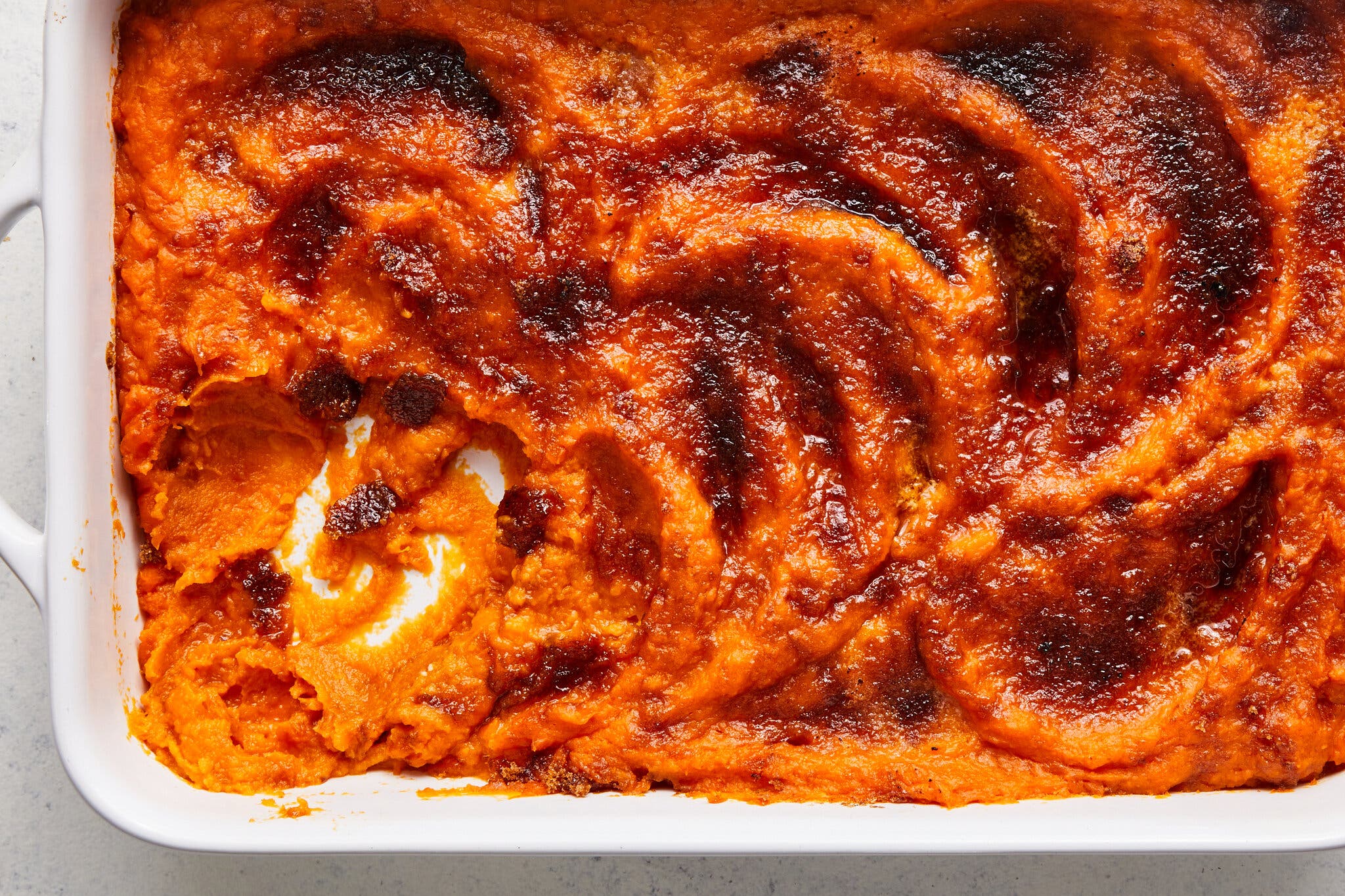 Bright orange sweet potatos in a baking dish with dark brown swirls of curry paste over the top.