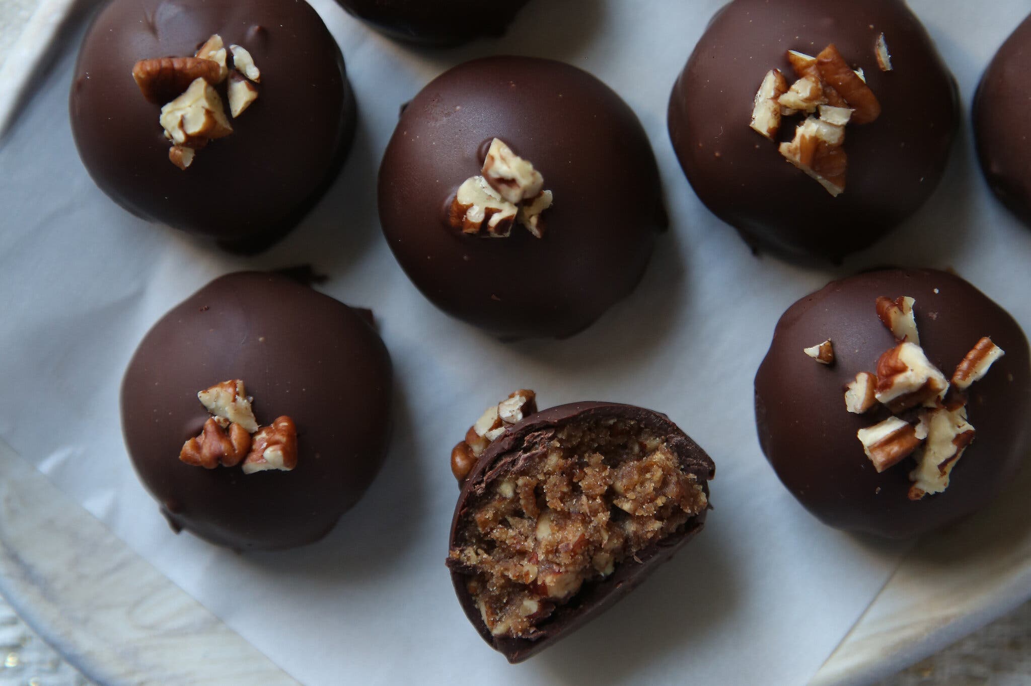 Several round, dark-chocolate-coated truffles, each garnished with pecan pieces. One is split, showing a nutty filling.