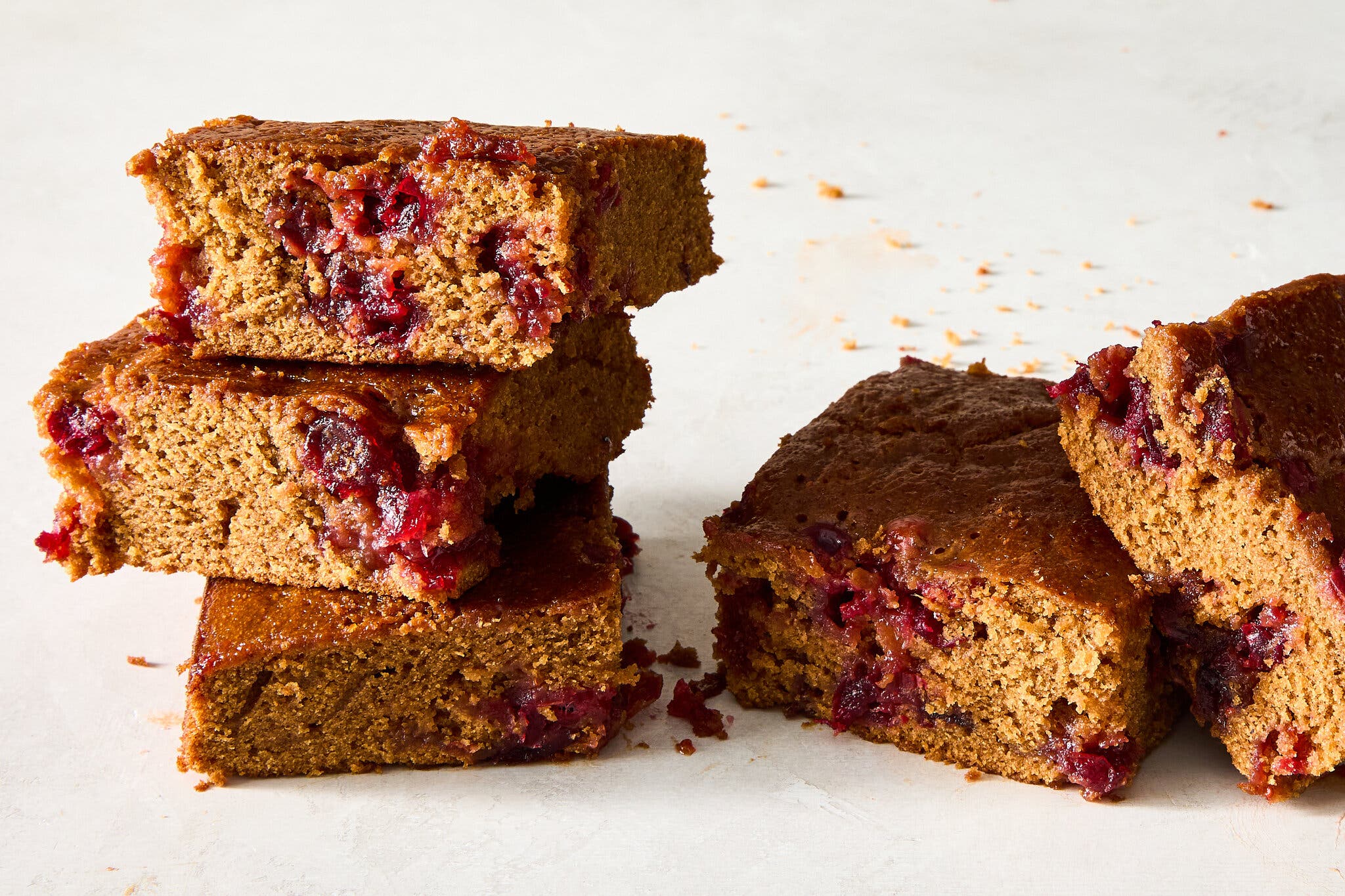 Five gingerbread bars studded with red cranberries, some stacked, sit on a light surface.